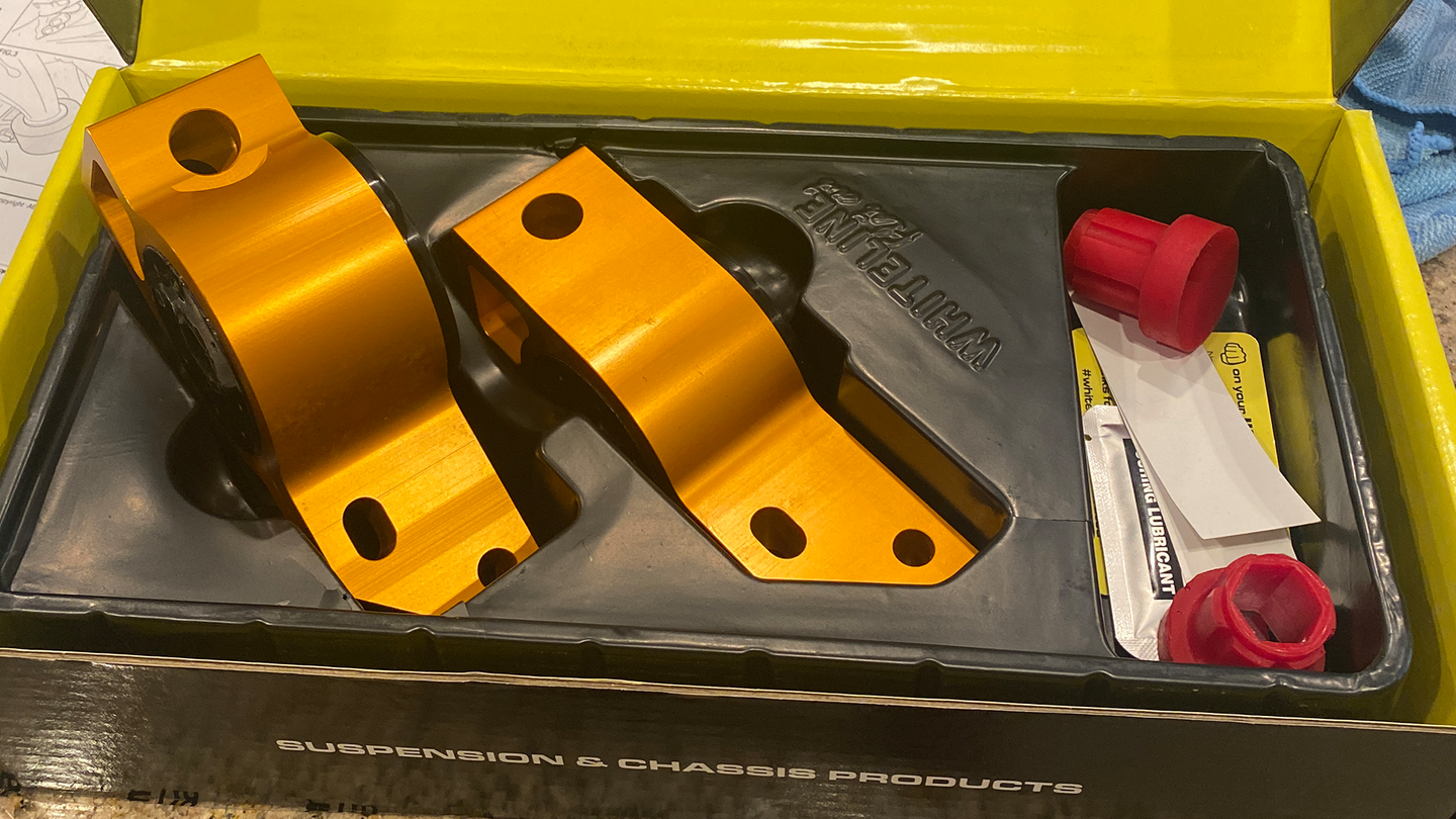An open box containing a pair of golden suspension parts. The lining of the box is black while the box itself is yellow.