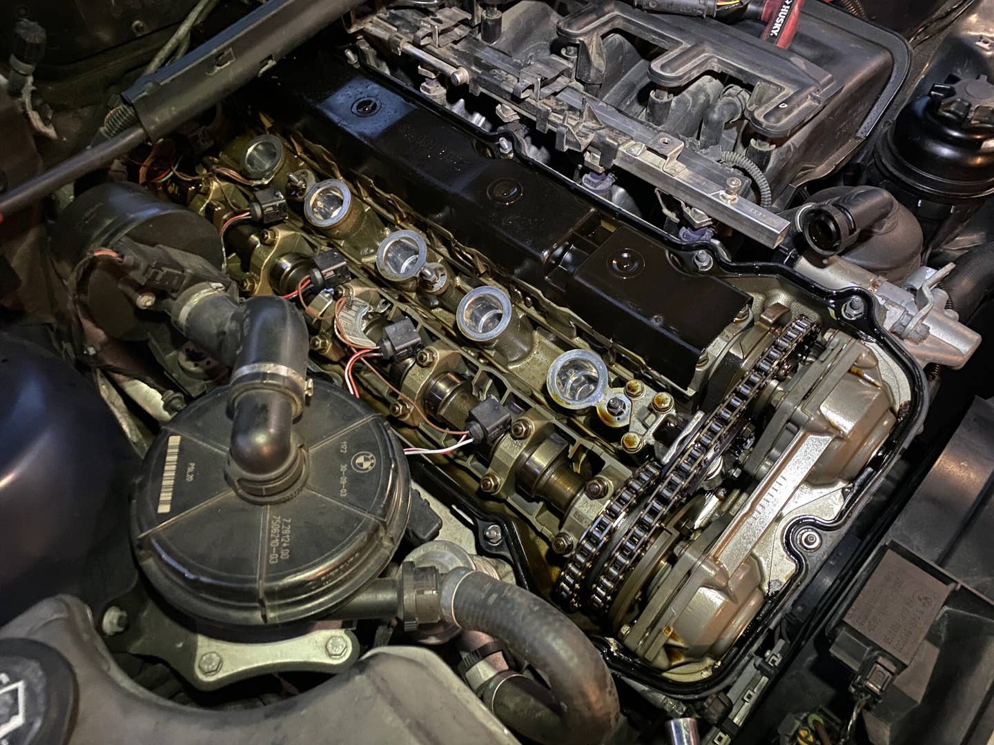 A BMW straight six engine with its valve cover removed, exposing a gold tinged valvetrain.