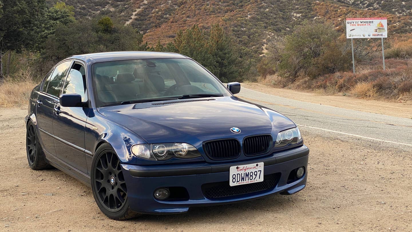 A blue BMW 330i ZHP parked on the side of a forested canyon road.