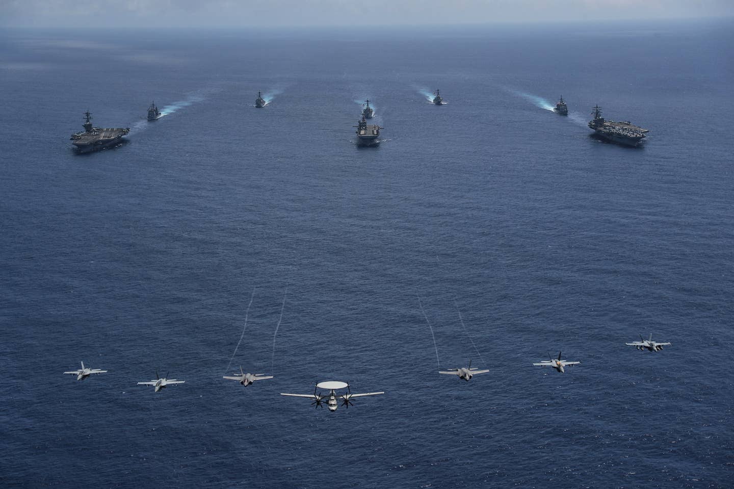 Aircraft from Carrier Air Wing Nine fly over the aircraft carrier <em>Abraham Lincoln</em> (CVN-72), front left, amphibious assault ship USS <em>Tripoli</em> (LHA-7), front center, aircraft carrier USS <em>Ronald Reagan</em> (CVN-76), front right, the cruiser USS <em>Mobile Bay</em> (CG-53), middle left, destroyer USS <em>Benfold</em> (DDG-65), middle center, cruiser USS <em>Antietam</em> (CG 54), middle right, destroyer USS <em>Spruance</em> (DDG-111), back left, and destroyer USS <em>Fitzgerald</em> (DDG-62), back right, as they sail in formation during Valiant Shield 2022. <em>U.S. Navy photo by Mass Communication Specialist 3rd Class Thaddeus Berry</em>