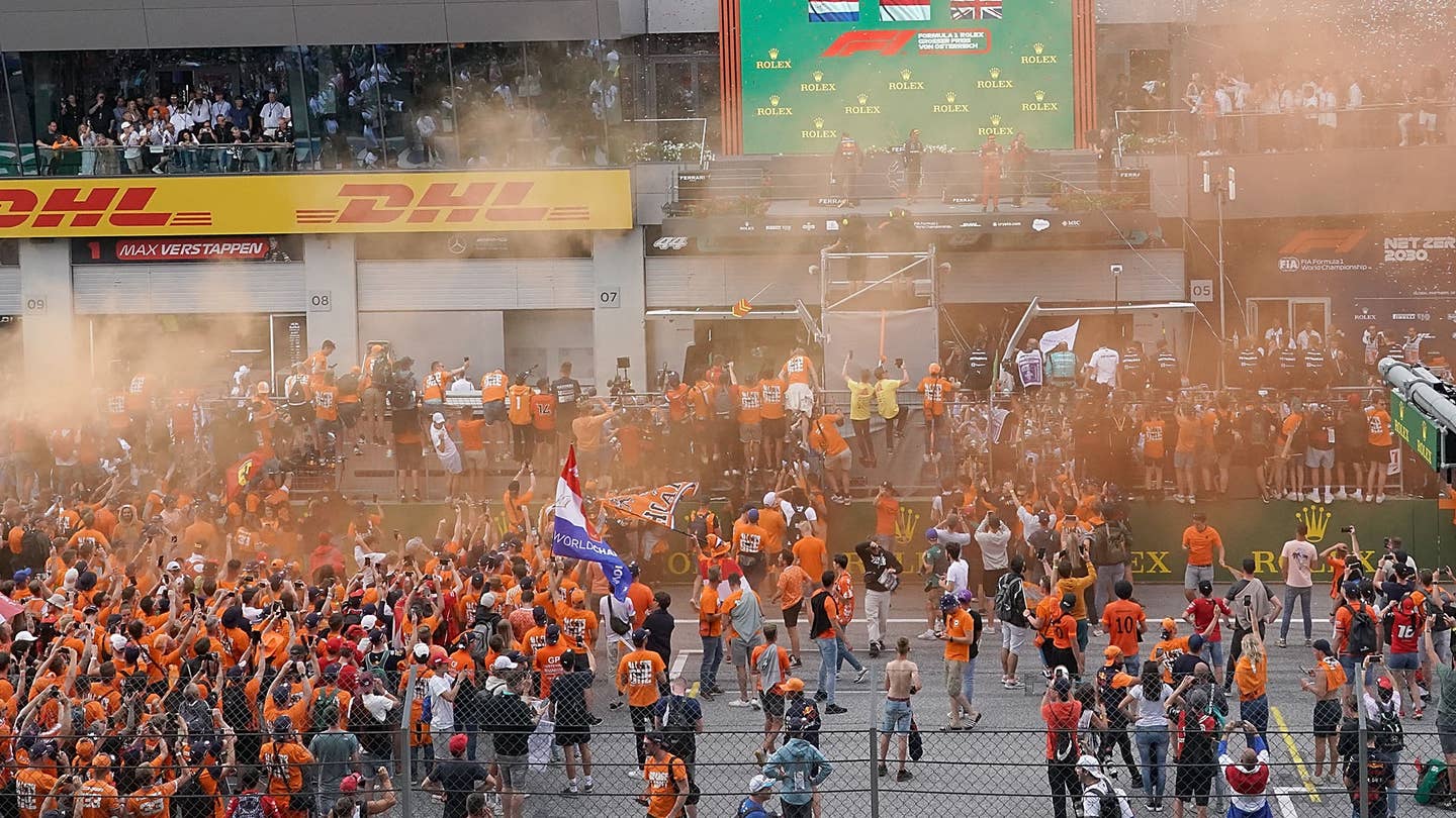 Fans gathering below the podium for the Austrian Grand Prix, wearing orange shirts and letting off orange flairs