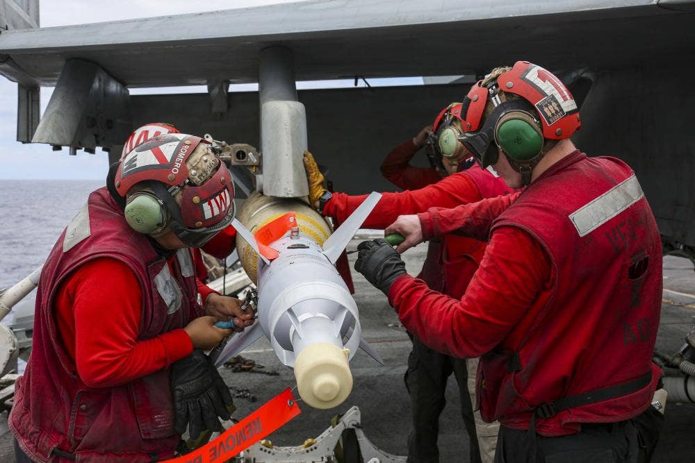 Ordnance crew from Strike Fighter Squadron 41 "Black Aces" (VFA-41) load a GBU-16 laser-guided bomb onto an F/A-18F Super Hornet on the USS <em>Abraham Lincoln</em>'s flight deck before a SINKEX at RIMPAC 2022. (DVIDS/MC3 Javier Reyes).