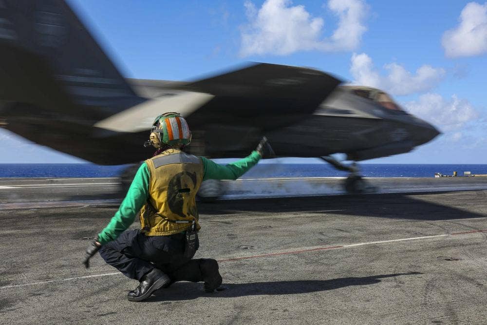 U.S. Navy Aviation Boatswain’s Mate (Equipment) 2nd Class Desiree Buttars, from Jacksonville, Fla., signals an F-35C Lightning II, assigned to the "Black Knights" of Marine Fighter Attack Squadron (VMFA) 314, as it launches from the flight deck of Nimitz-class aircraft carrier USS Abraham Lincoln (CVN 72) for a sinking exercise. <em>Credit: Mass Communication Specialist 3rd Class Javier Reyes/U.S. Navy</em>