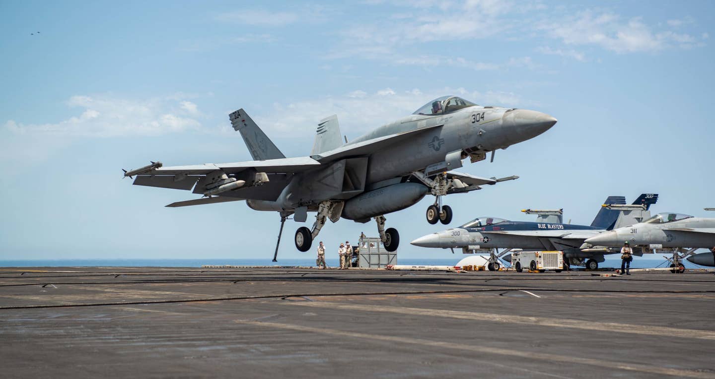 An F/A-18E Super Hornet lands on the USS <em>Harry S. Truman</em> in June 2022. This aircraft has an inert version of the AIM-120 Advanced Medium Range Air-to-Air missile under its left wing and what may also be a training version of the AIM-9X Sidewinder on the wingtip. <em>US Navy / Mass Communication Specialist 2nd Class Kelsey Trinh</em>