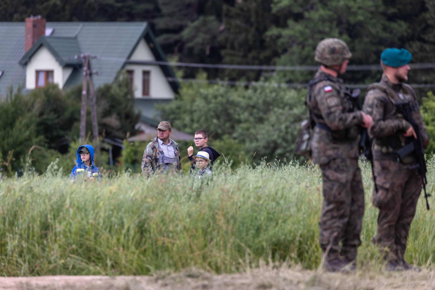 A local family stands in their field to watch as the Polish and Lithuanian president address a press conference following a joint visit of the NATO Multinational Division North East mobile command center near Szypliszki village, located in the so-called Suwalki Gap, on July 7, 2022. <em>Photo by WOJTEK RADWANSKI/AFP via Getty Images</em>