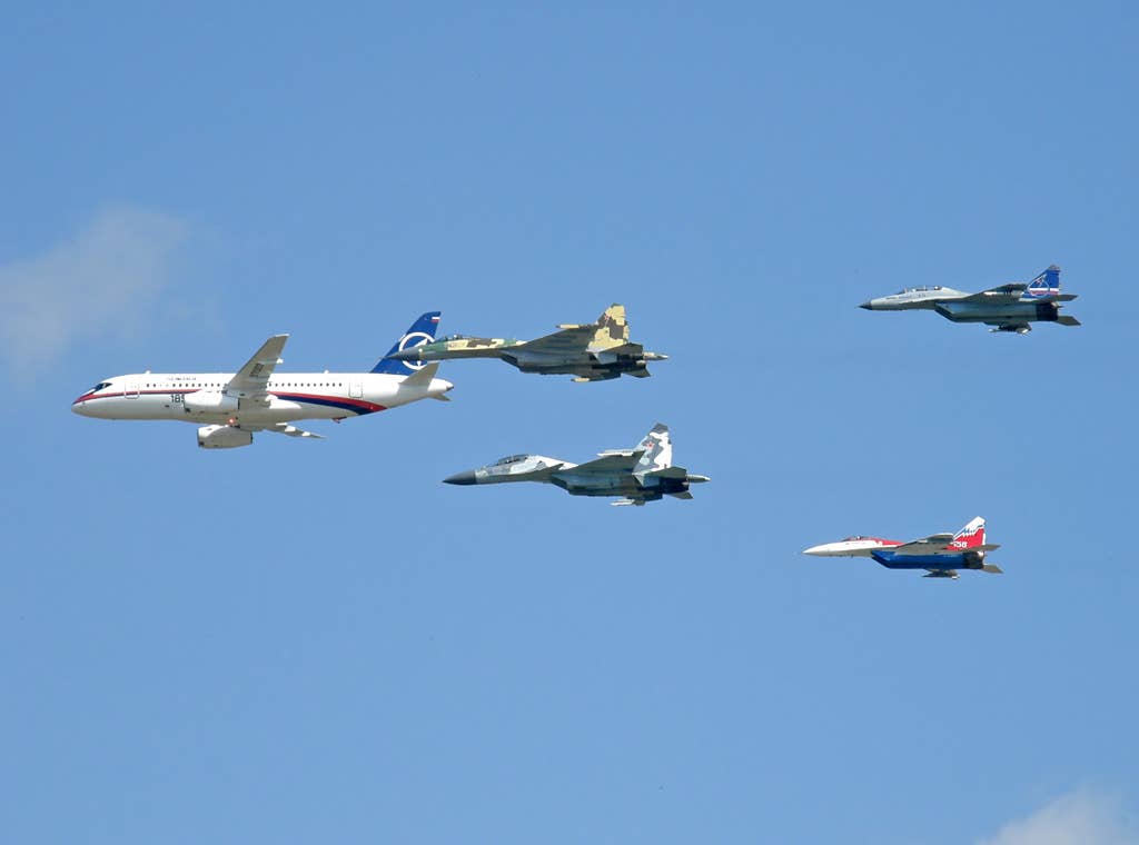 A Sukhoi Superjet 100 regional airliner leads a formation of Su-35 (second row, nearest camera) and Su-30MKM (second row, furthest from camera), followed by a MiG-35 and a MiG-29M-OVT, in August 2009. <em>Dmitry Terekhov/Wikimedia Commons</em>