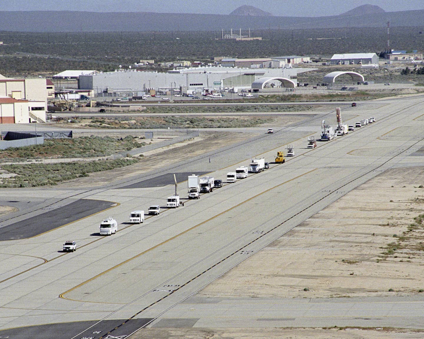 A long string of specialized NASA vehicles convoys down a taxiway at Edwards Air Force Base to begin a Space Shuttle rescue and recovery training exercise.