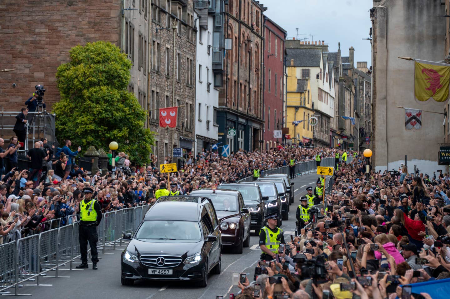 EDINBURGH, SCOTLAND - SEPTEMBER 11:  People gather in tribute as the cortege with the hearse carrying the coffin of the late Queen Elizabeth II, draped with the Royal Standard of Scotland, passes down the Royal Mile, Edinburgh, on the journey from Balmoral to the Palace of Holyroodhouse on September 11, 2022 in Edinburgh, United Kingdom. Elizabeth Alexandra Mary Windsor was born in Bruton Street, Mayfair, London on 21 April 1926. She married Prince Philip in 1947 and ascended the throne of the United Kingdom and Commonwealth on 6 February 1952 after the death of her Father, King George VI. Queen Elizabeth II died at Balmoral Castle in Scotland on September 8, 2022, and is succeeded by her eldest son, King Charles III.  (Photo by Andrew O'Brien/WPA Pool/Getty Images)