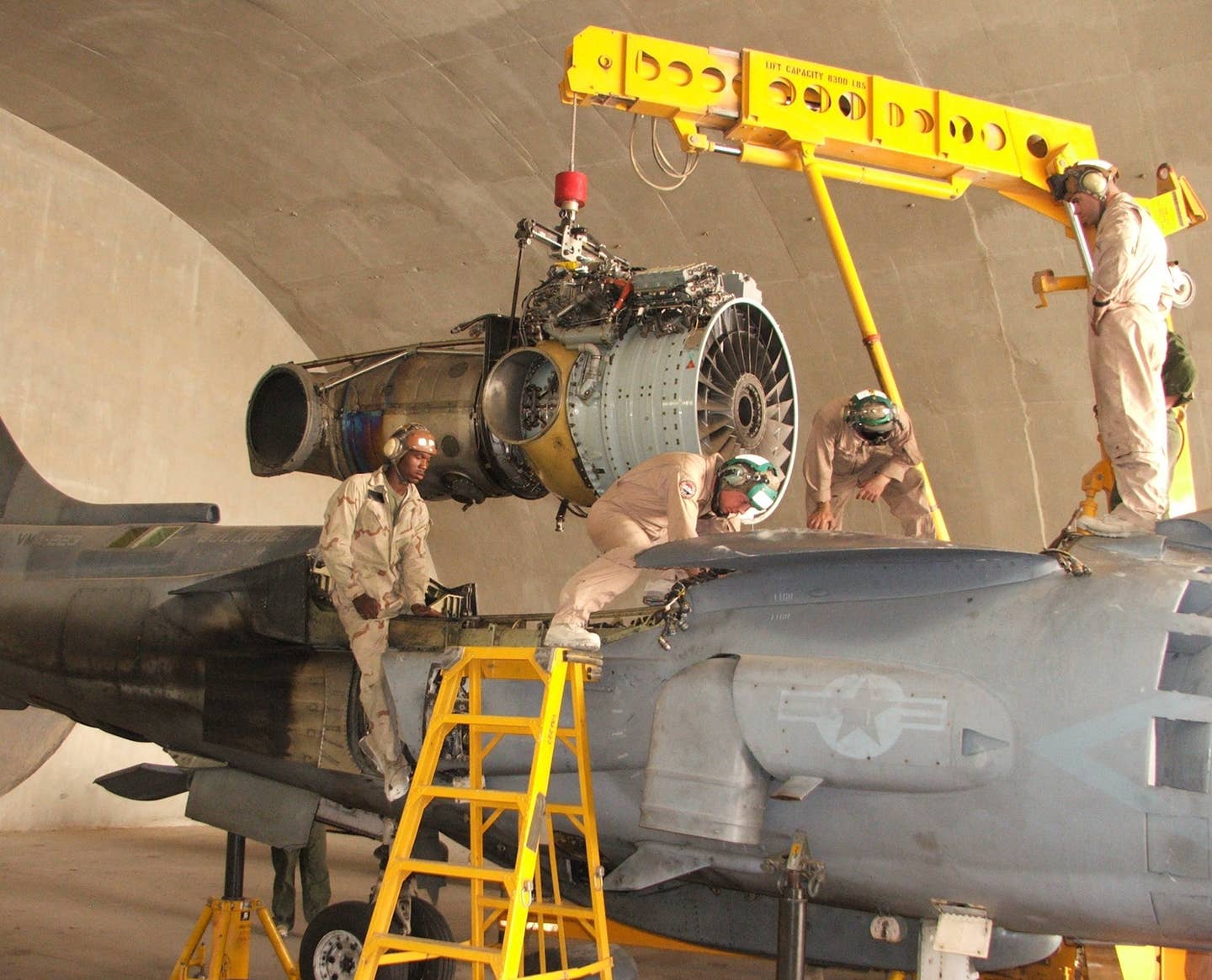 Marines with Marine Attack Squadron 223 (VMA-223) change the engine on an AV-8B Harrier II. In this image, the forward nozzle is deflected fully downward, while the rear nozzle is deflected fully backward for forward flight. <em>U.S. Marine Corps</em>