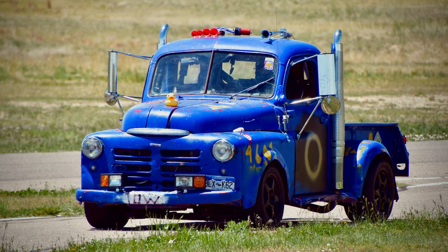 A blue 1950 Dodge pickup with exhaust stacks against a grassy backdrop