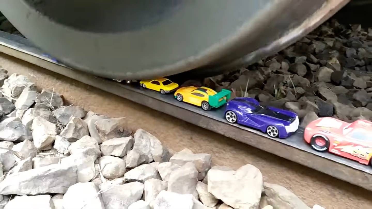 A train wheel crushes a series of toy cars left on the rail