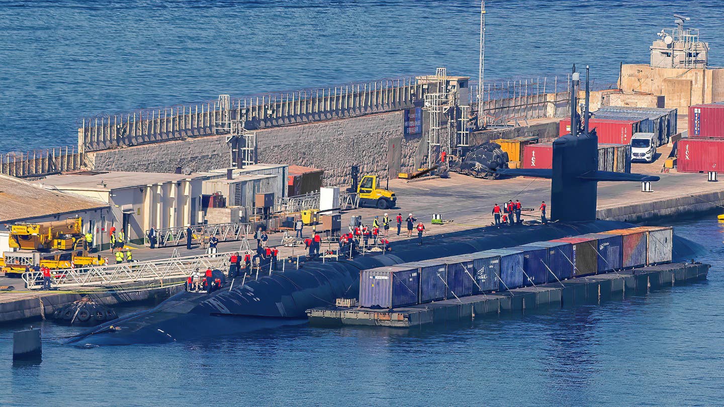 A Mexeflote&nbsp;barge loaded with shipping containers is seen here positioned alongside the hull of USS <em>Rhode Island</em> at His Majesty's Naval Base Gibraltar. <em>William Jardim</em>