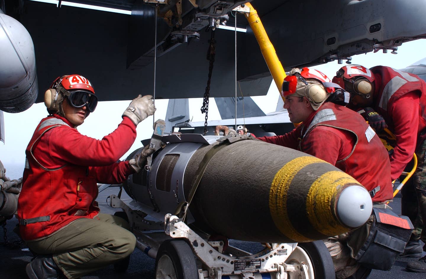 Aviation ordnancemen load a 2,000-pound Joint Direct Attack Munition (JDAM) onto an F/A-18 Hornet fighter jet aboard the aircraft carrier USS <em>John C. Stennis</em>, while conducting combat missions in support of Operation Enduring Freedom. <em>U.S. Navy photo by Photographer’s Mate 3rd Class Alta I. Cutler</em>