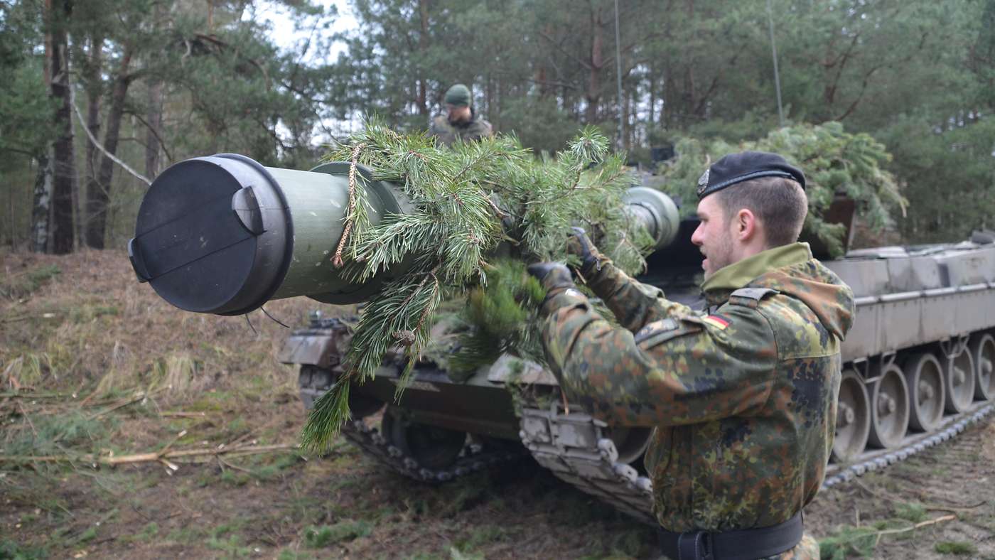 The commander of a German Army Leopard 2A6M checks the camouflage and ensures the functionality and safety of the main gun while on exercise. <em>Bundeswehr/Andre Schmidt</em>