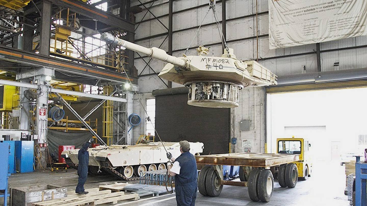 Workers maneuver the turret from an M1 Abrams tank during maintenance. <em>U.S. Army</em>