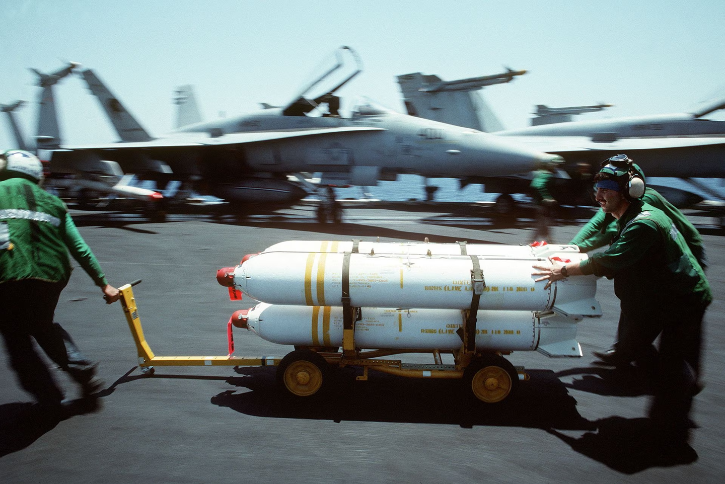 Maintenance crewmen from Attack Squadron 34 move a weapons skid loaded with Mk 20 Rockeye II cluster bombs across the flight deck of the nuclear-powered aircraft carrier USS<em> Dwight D. Eisenhower</em> in 1990. <em>Credit: U.S. Navy</em>