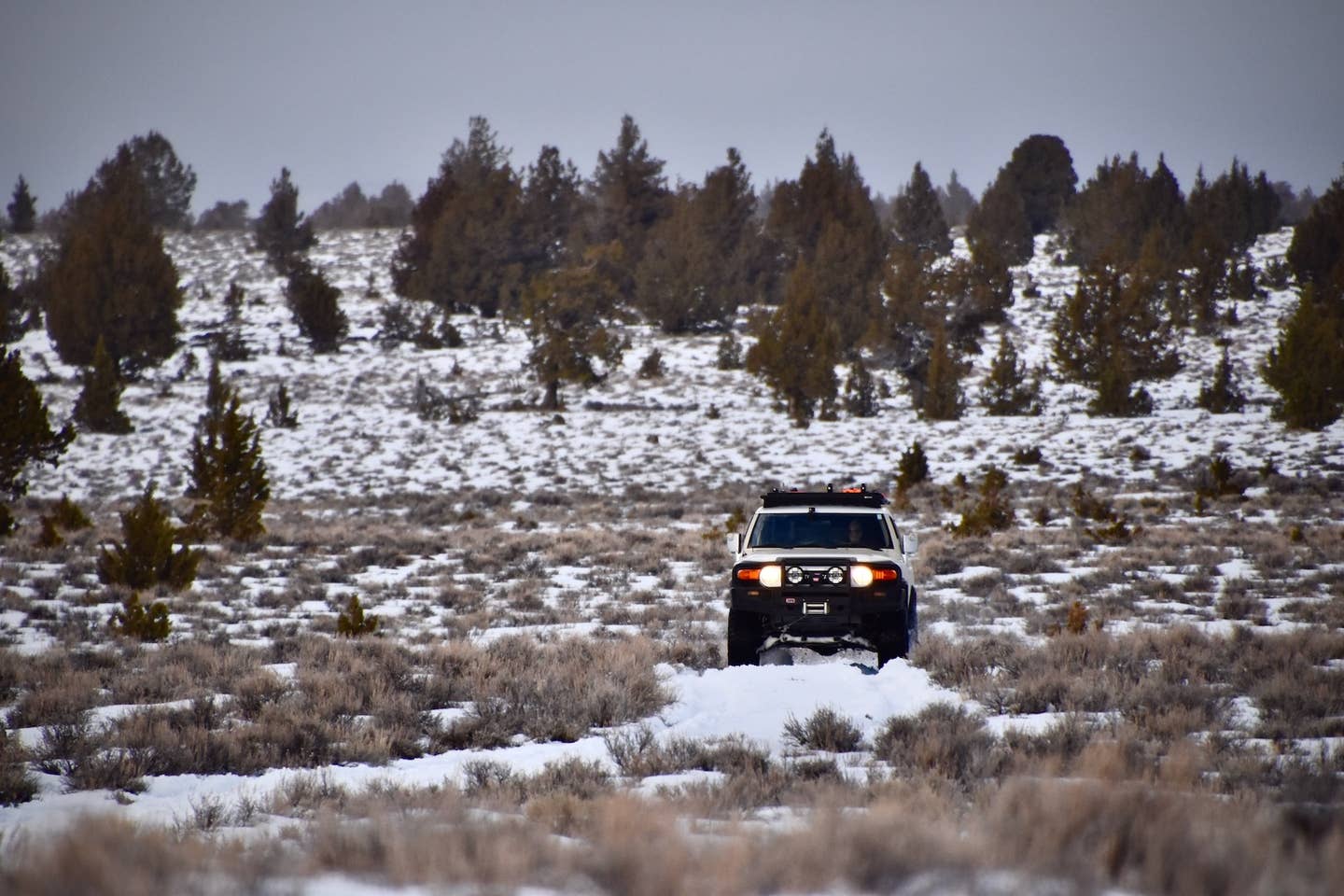 A Toyota FJ Cruiser traverses snowy plains in fading light