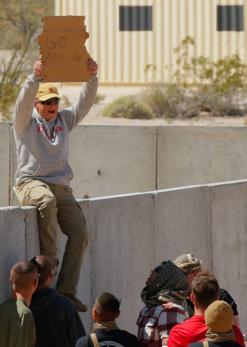 A role player perched on the wall of the mock consulate compound holds a sign reading "GO AWAY USA." <em>USMC</em>