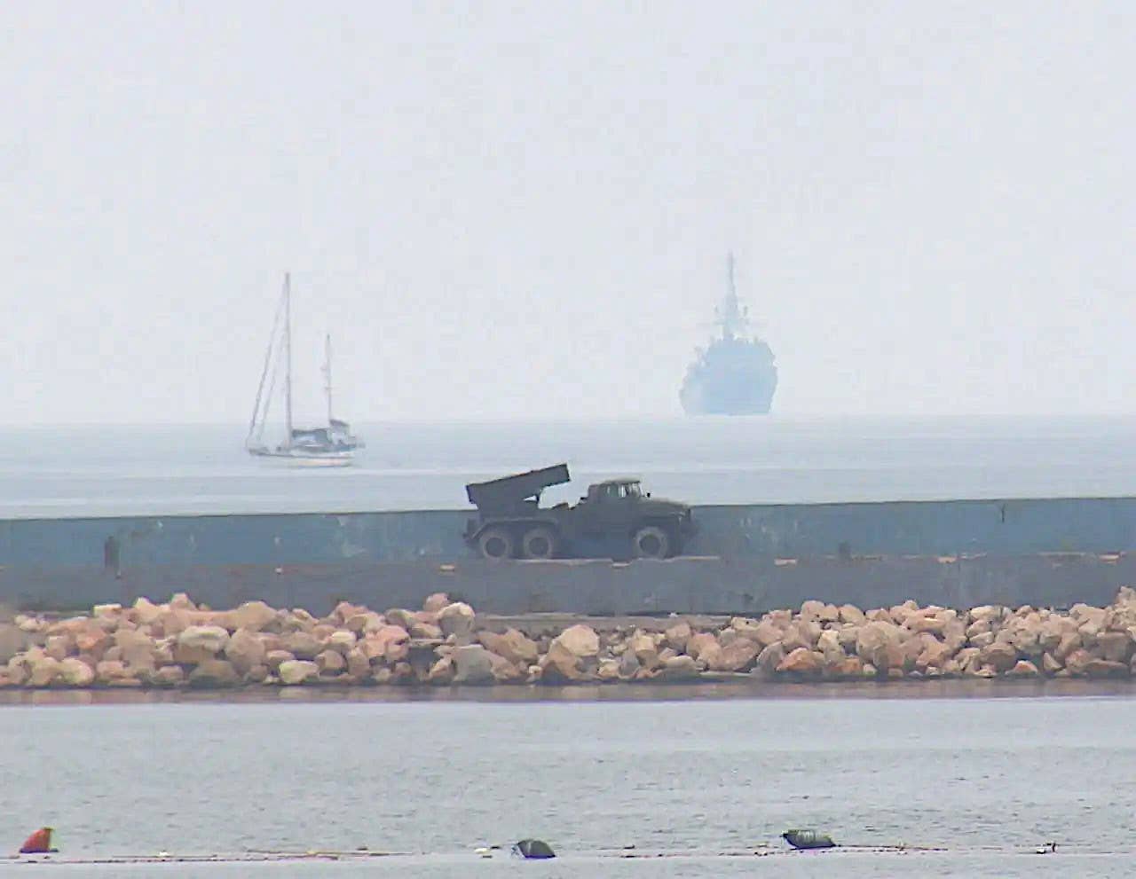 The BM-21, or variant thereof, positioned along the seawall at the mouth of Sevastopol Bay. A section of a floating boom strung across the entrance to the harbor can be seen at the bottom of the picture. What the Russian Navy's Black Sea Fleet said was the Project 18280&nbsp;<em>Yuriy Ivanov&nbsp;</em>class intelligence ship&nbsp;<em>Ivan Khurs</em> returning to port after the recent drone boat attack is seen at the top right. <em>Russian Navy Black Sea Fleet</em>