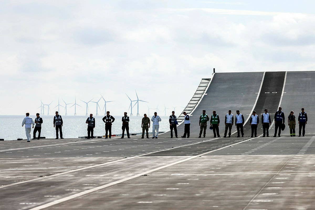 Royal Navy personnel carry out a foreign object damage (FOD) walk to check the flight deck of the HMS <em>Prince of Wales </em>before flying operations commence. <em>Crown Copyright</em>