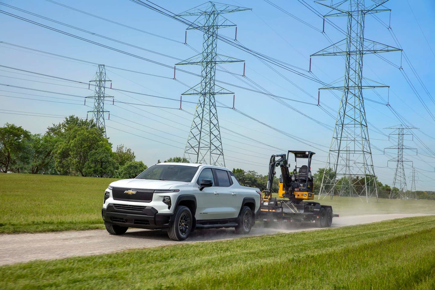 The Silverado EV WT kicking up dust while towing heavy machinery.