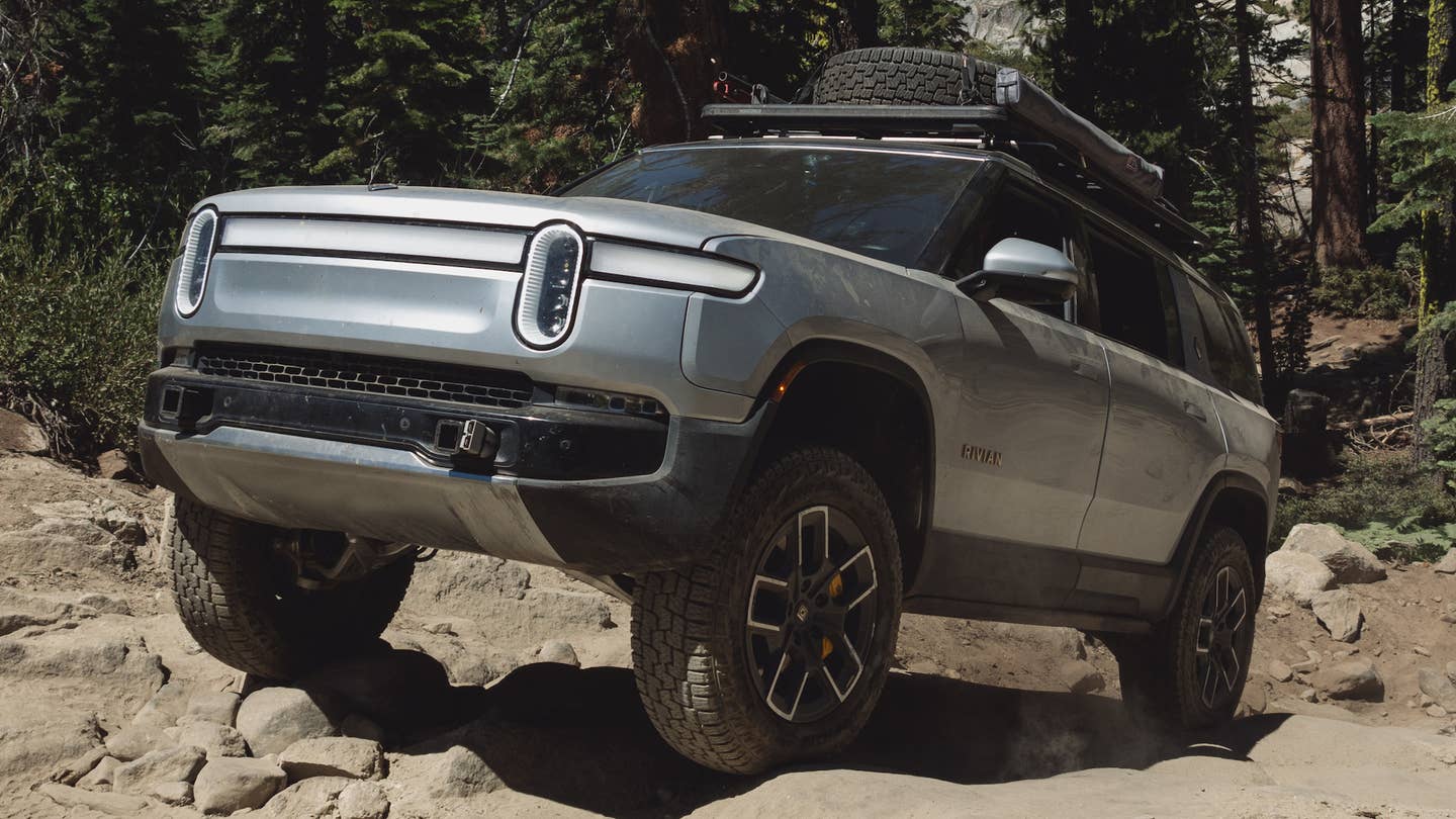 Rivian R1S SUV in silver, driving uphill on a trail