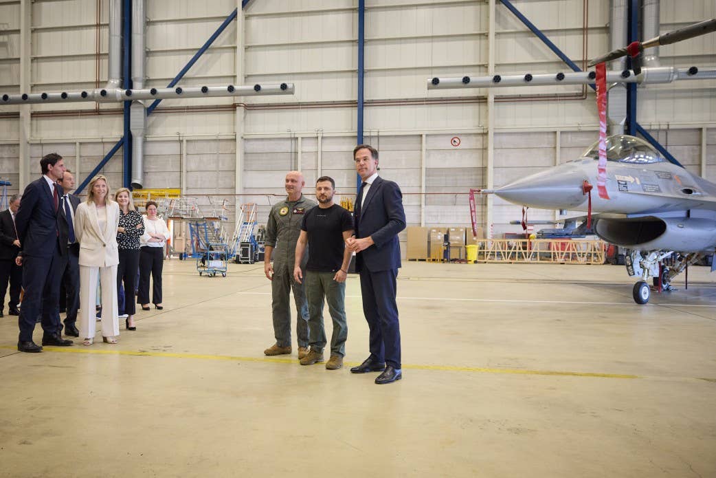 Ukrainian President Volodomyr Zelensky (center) and Dutch Prime Minister Mark Rutte (l) pose in front of a Royal Netherlands Air Force F-16 at the Eindhoven Air Base. (Ukrainian President's Office photo)