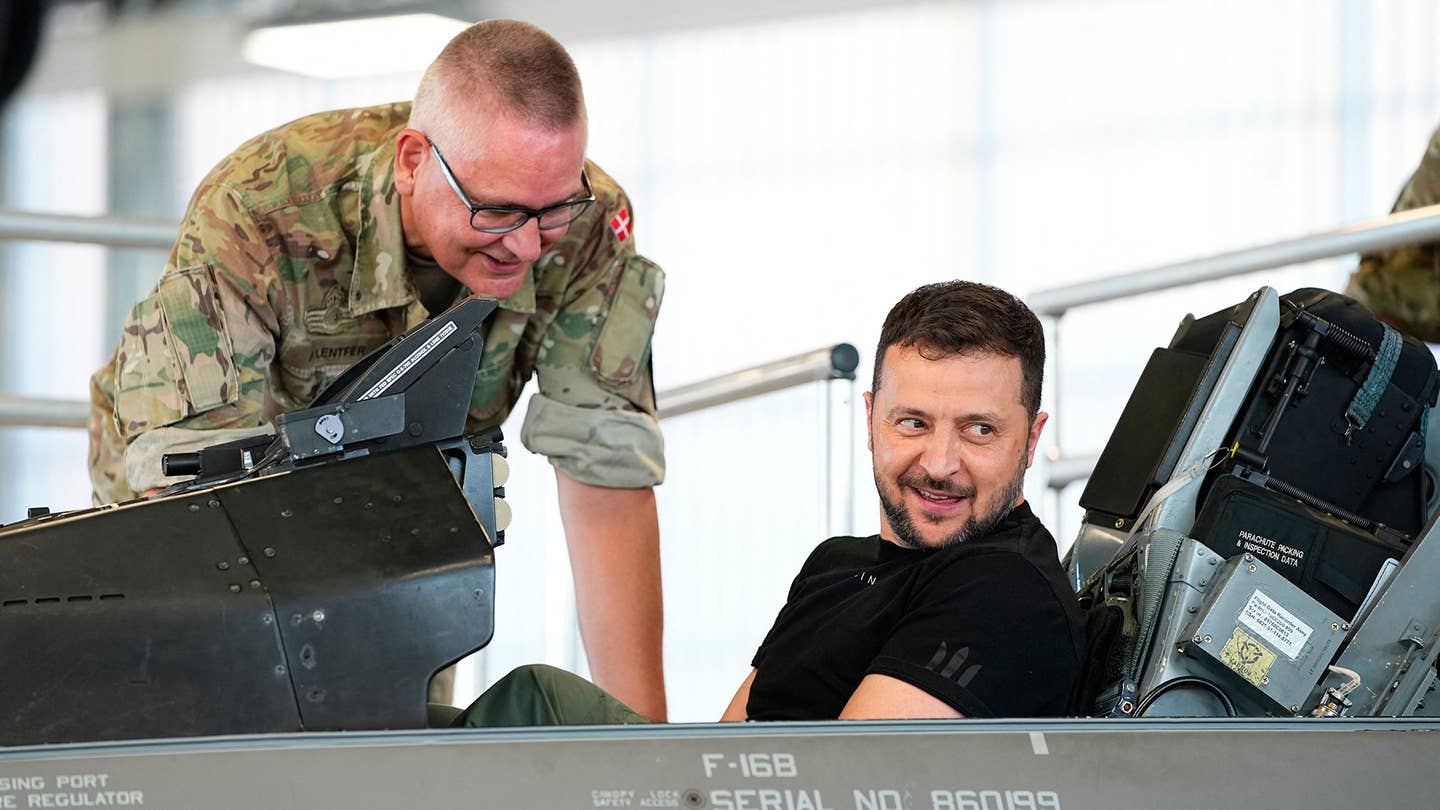 Ukrajinský prezident Volodymyr Zelenskyj (R) reaguje, když 20. srpna 2023 sedí ve stíhačce F-16 v hangáru letecké základny Skrydstrup ve Vojens v severním Dánsku. (Foto MADS CLAUS RASMUSSEN/Ritzau Scanpix/AFP přes Getty Snímky)