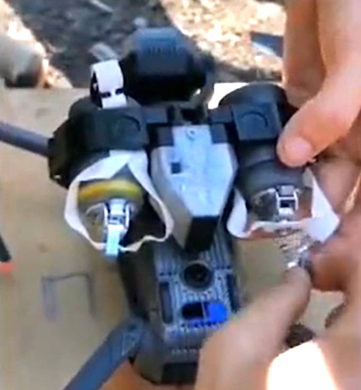A screen capture showing M42/M46 submunitions loaded onto a drone. The temporary safety tab used in this conversion process is being removed from the one on the right, but is still visible in place on the one on the left. <em>capture via Twitter</em>