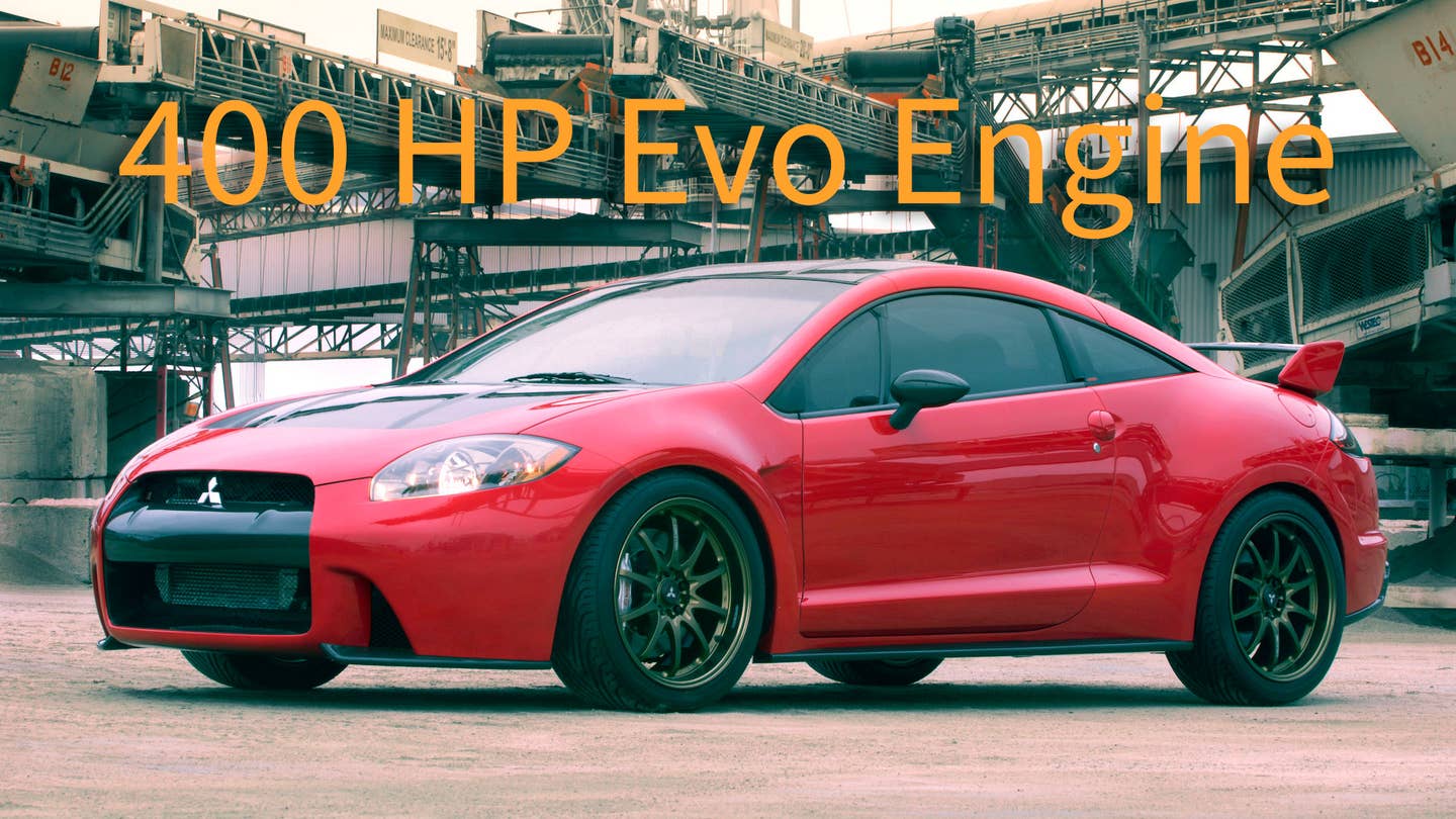 2005 Mitsubishi Eclipse Ralliart Concept. A red couple with a black grille and a large rear spoiler sits low to the ground against a background of an industrial facility.