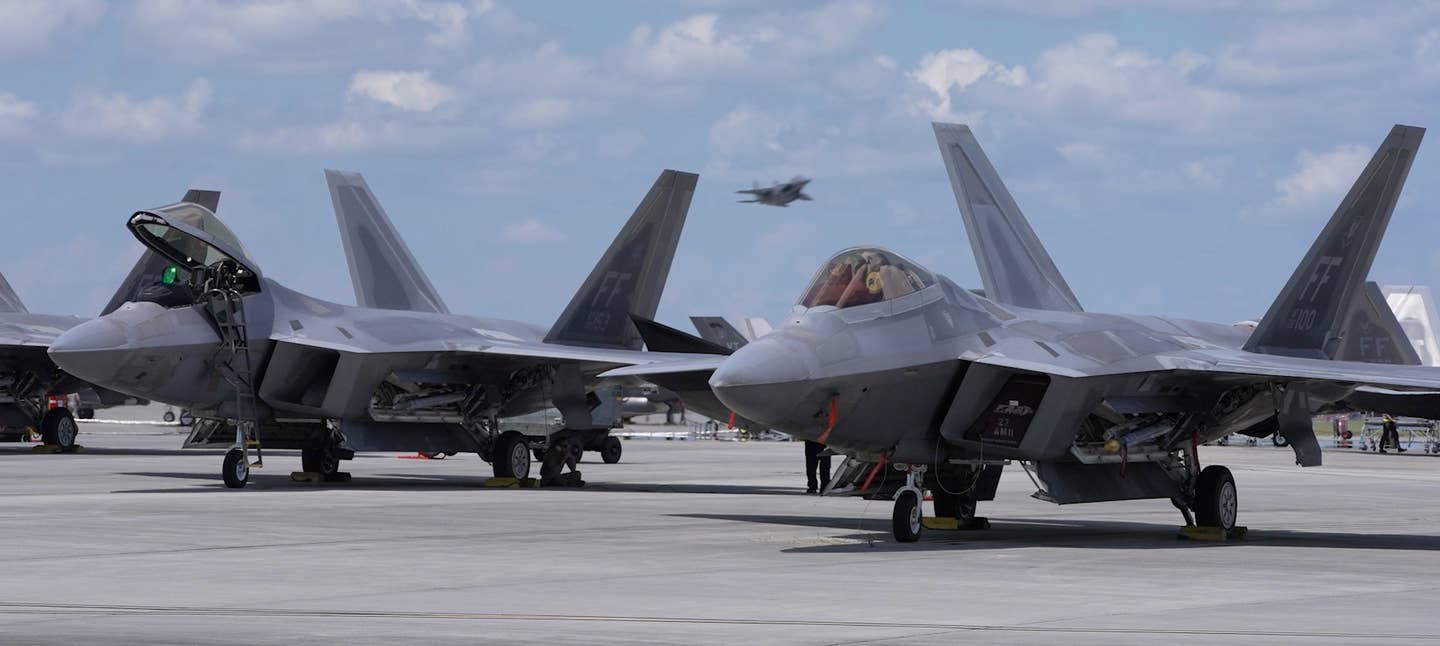 A pair of Langley-based F-22As sit on the ramp as an F-15E Strike Eagle departs on a William Tell mission. <em>Jamie Hunter</em>