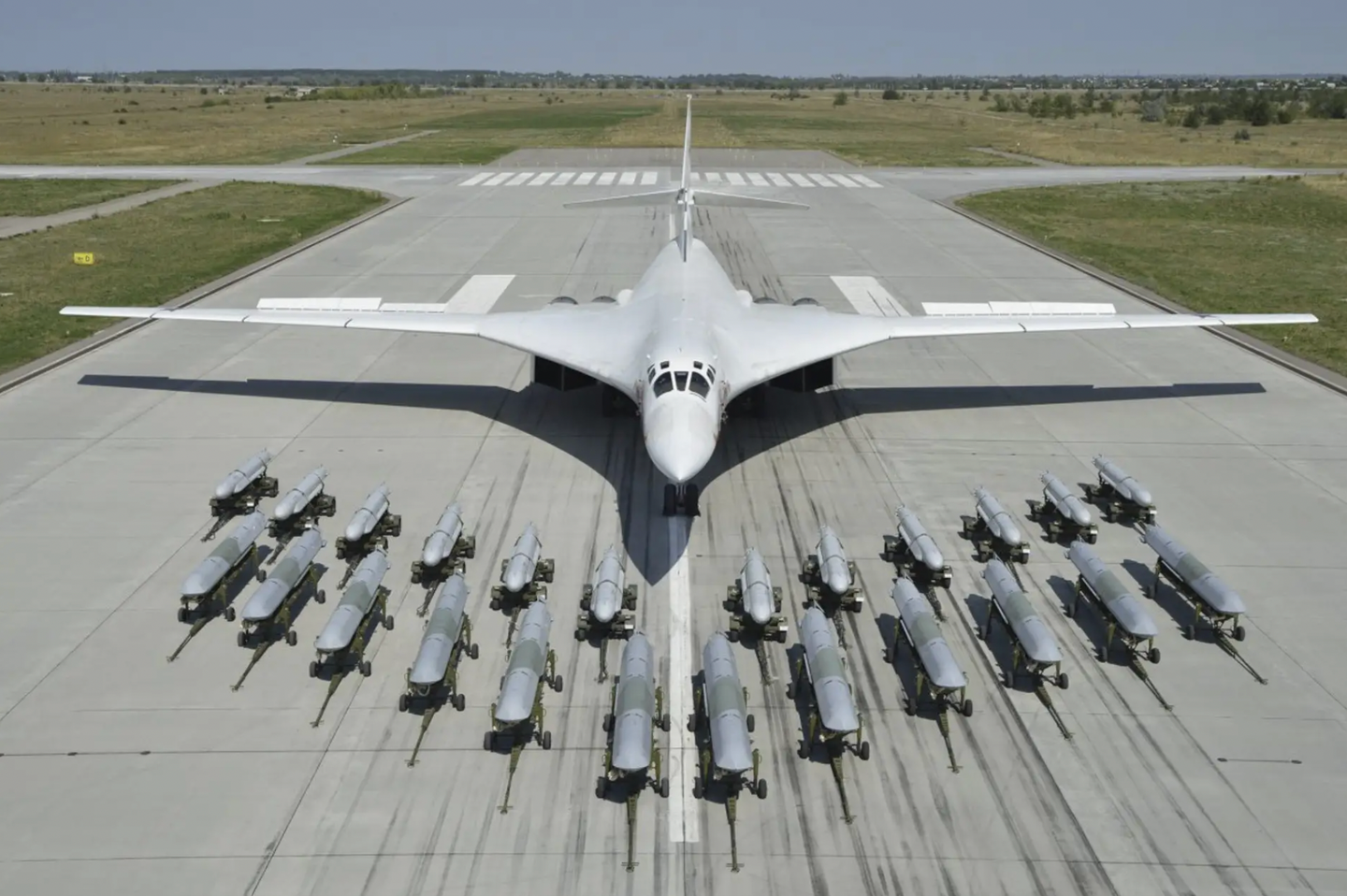 A row of 12 Kh-101/102-series air-launched cruise missiles, in front, and another dozen of the earlier Kh-55-series missiles behind them, on display with a Tu-160 Blackjack bomber in the background.&nbsp;<em>Russian Ministry of Defense</em>