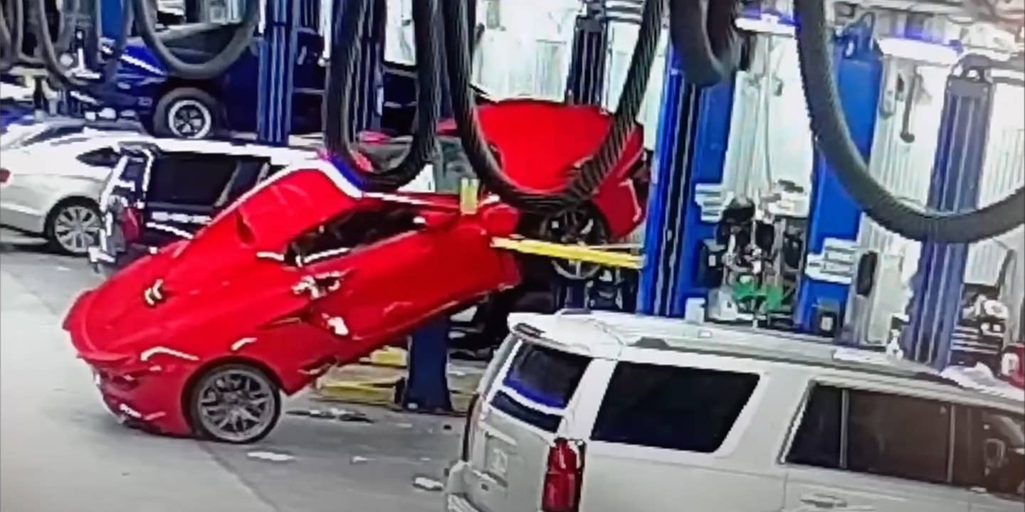 A red Chevrolet Corvette Z06 teetering off a garage lift after it has fallen.
