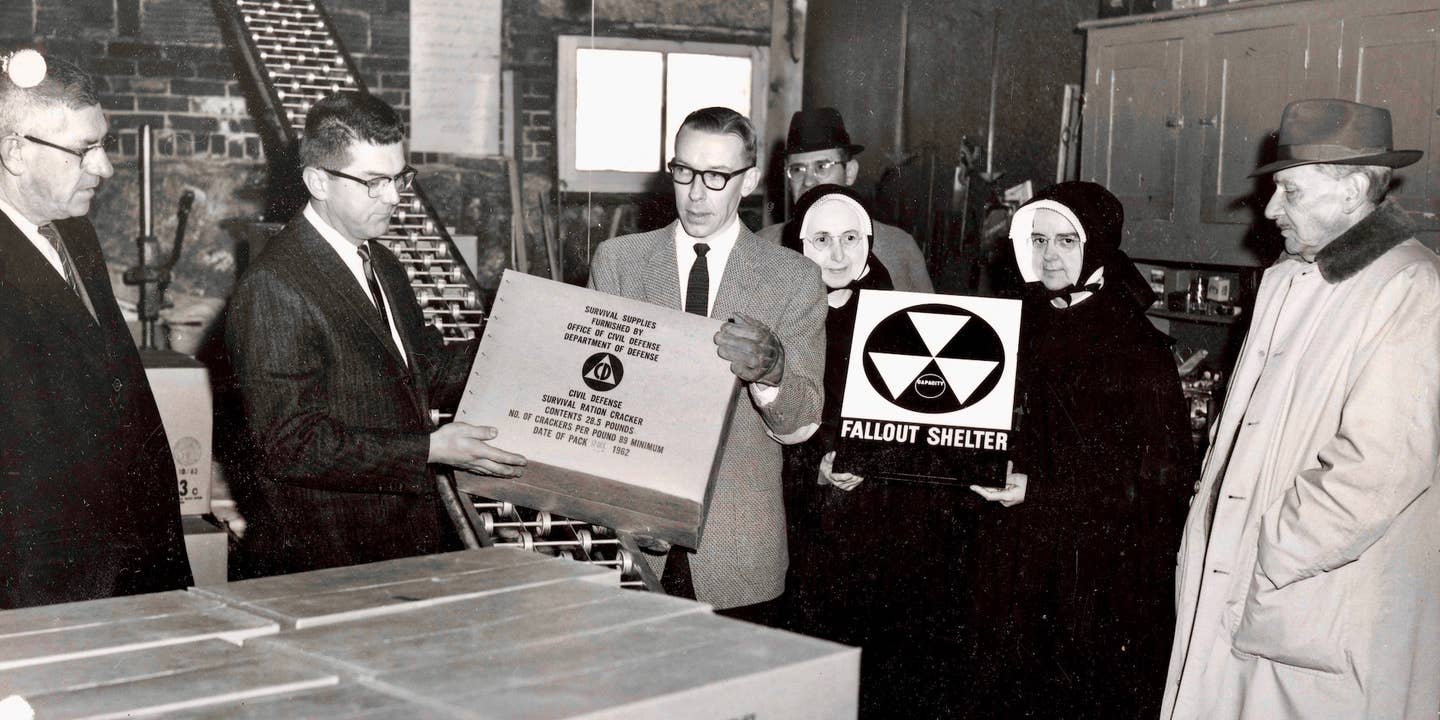 This photograph depicts a fallout shelter being furnished with Civil Defense survival rations at Villa Augustina Academy in Goffstown, New Hampshire. Mother Wilfred and Mother Superior Liguori of the Religious of Jesus and Mary, the religious order that founded and operated the school, appear in the photograph, holding a fallout shelter sign.