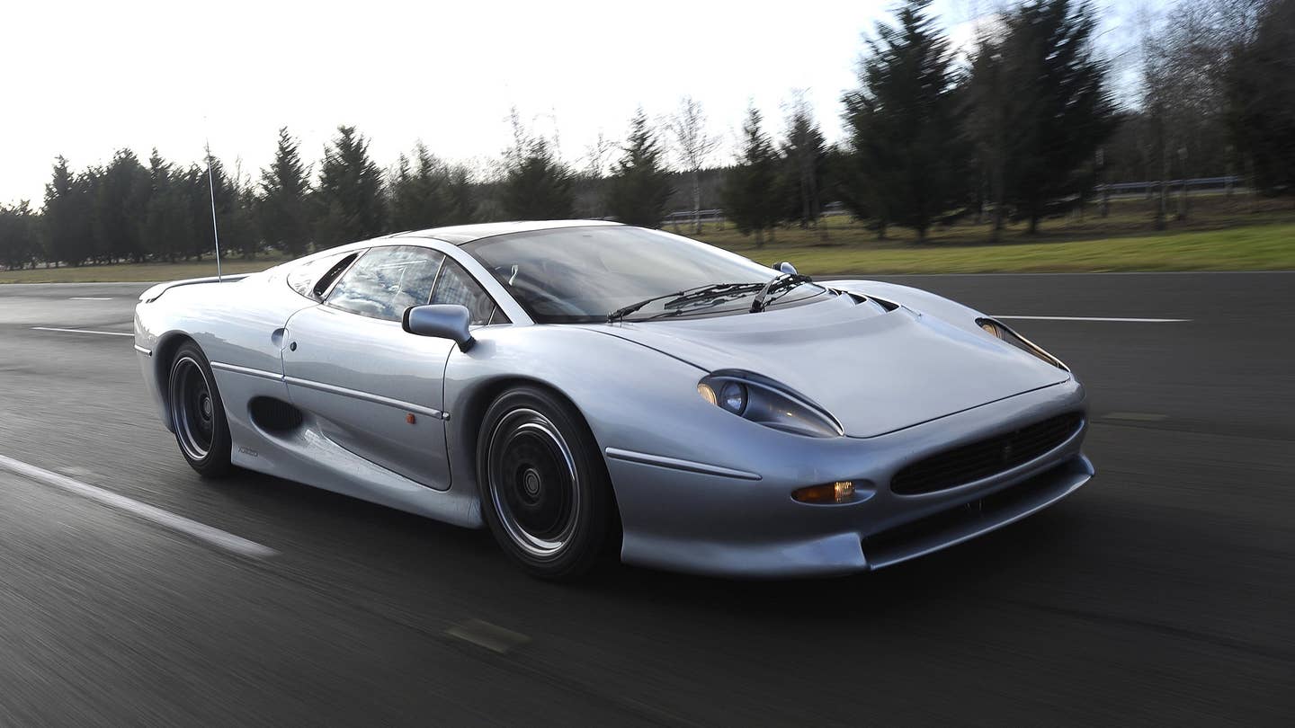 Jaguar XJ220 in silver driving on road photographed from front three-quarter angle.
