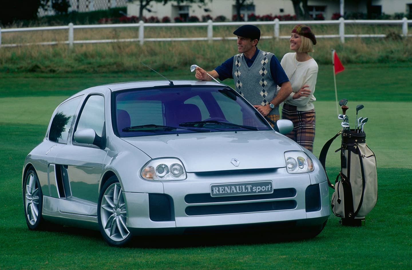 Press photo of Renault Clio V6 on golf course with golfers posed near car.