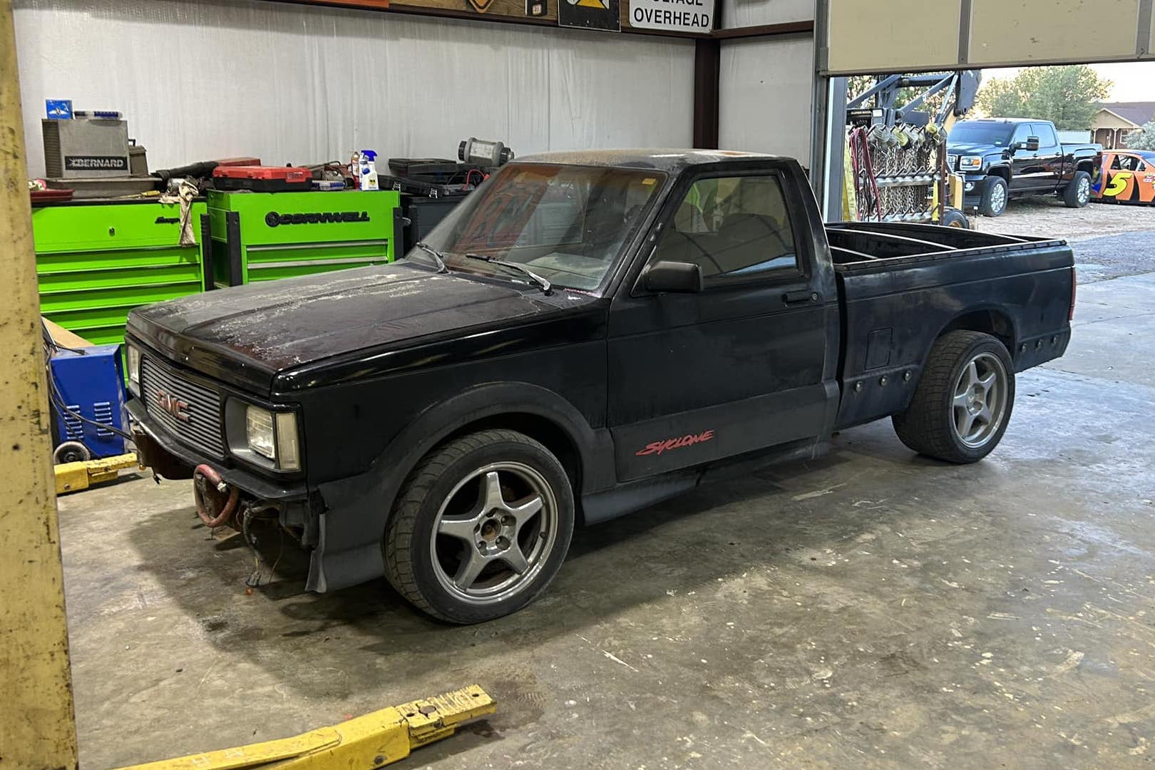 GMC Syclone without its front bumper, sitting in a garage bay with a lift