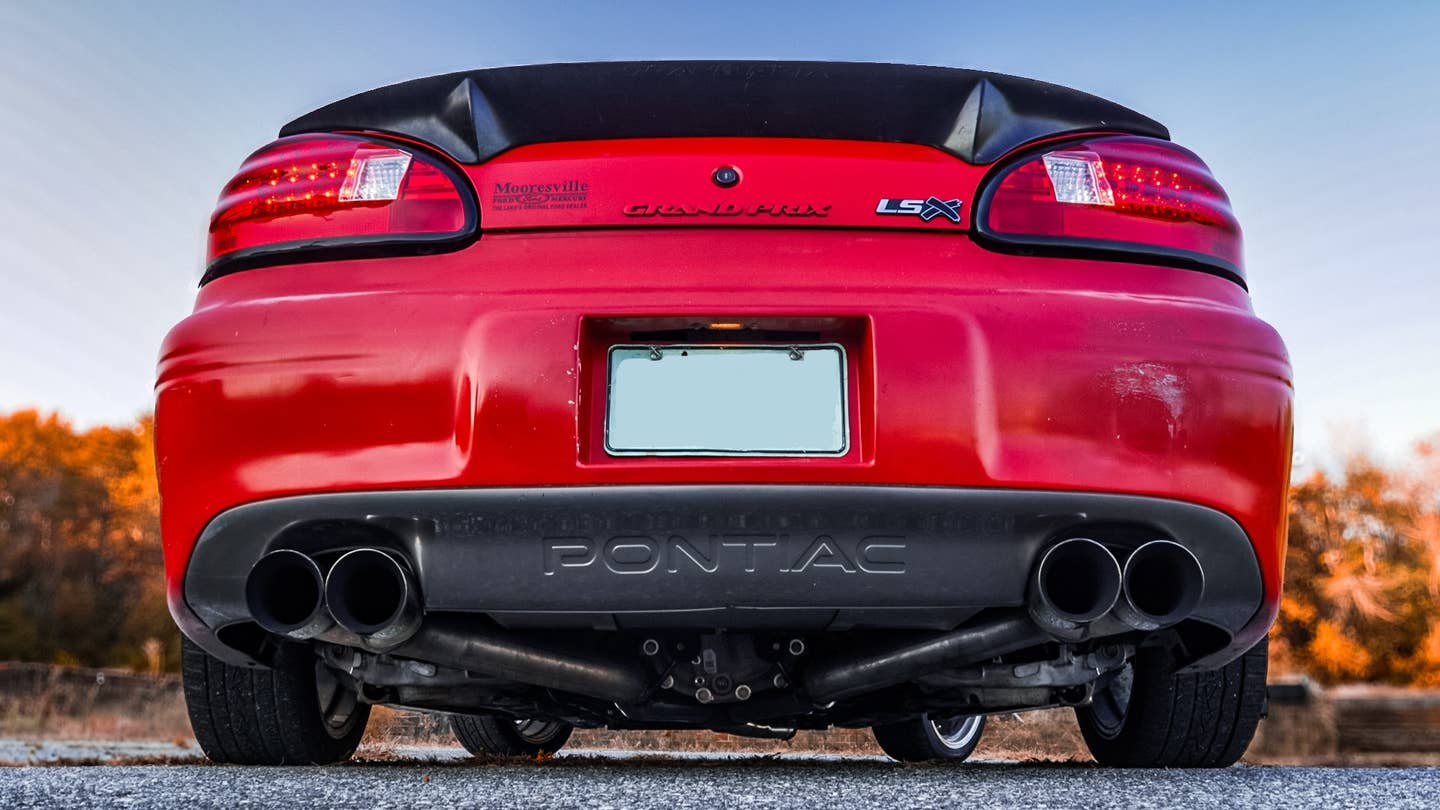 Tyler Pitman's rear-wheel-drive, V8-swapped 1999 Pontiac Grand Prix, from low and behind. Four exhaust tips poke out from under a rear bumper topped by a large spoiler.