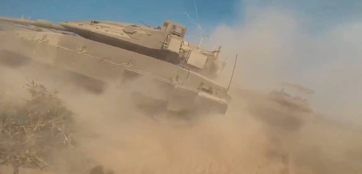 Zatímco bojovník Hamasu běží k izraelskému tanku Merkava, hlaveň dalšího z nich míří jeho směrem.  (Obrazovka Hamasu)