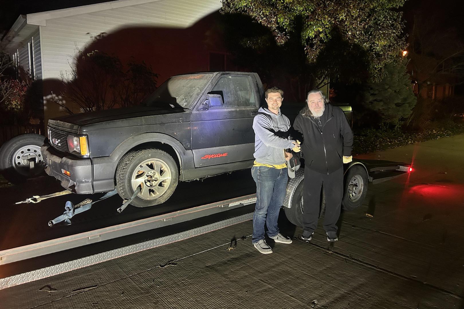 George Bowman and Jake Rowe shake hands next to a black GMC Syclone pickup truck on a trailer