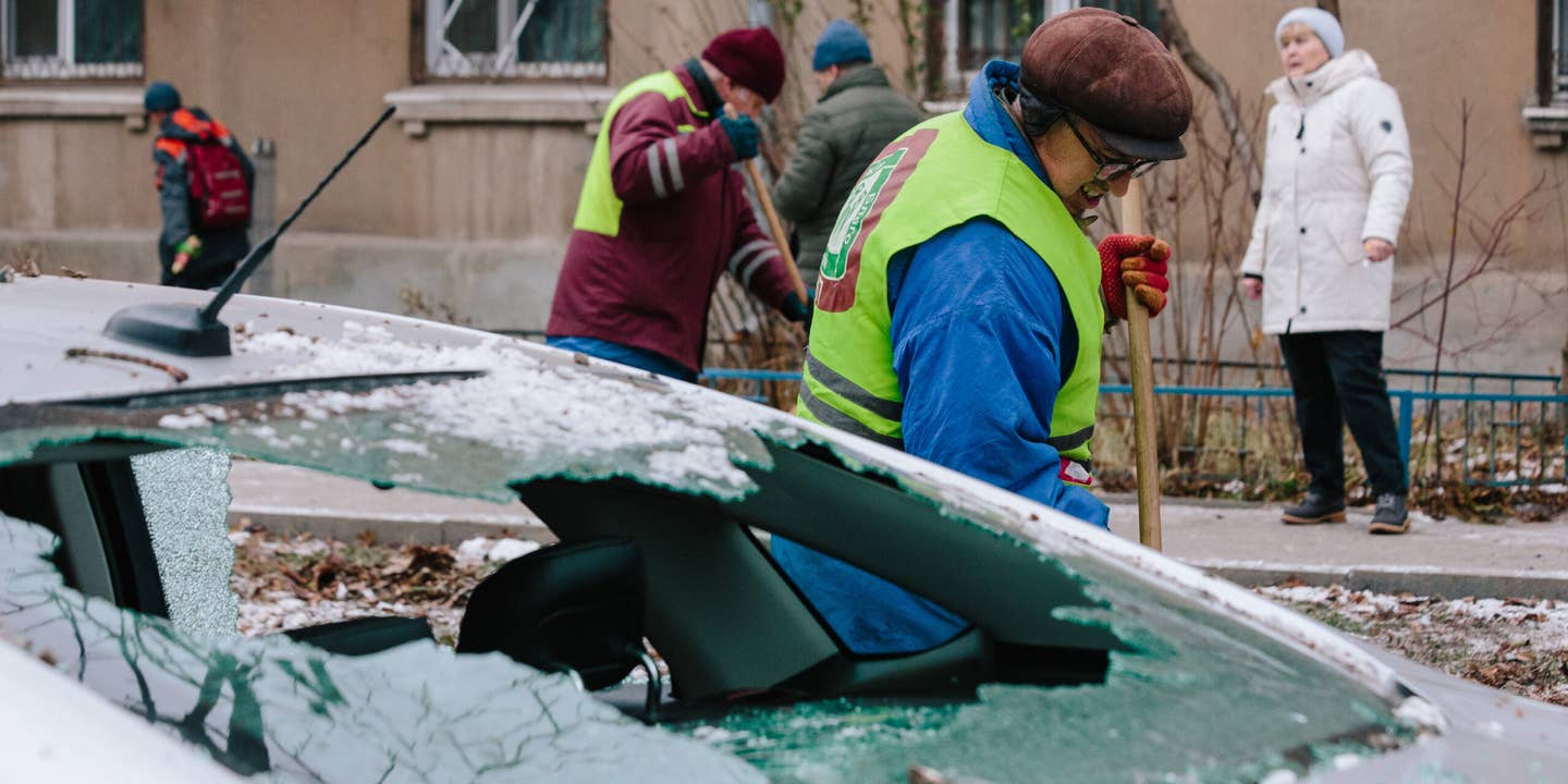 Utility workers are cleaning up the aftermath of an attack against the backdrop of a damaged car, in Kharkiv, Ukraine, on December 8, 2023.