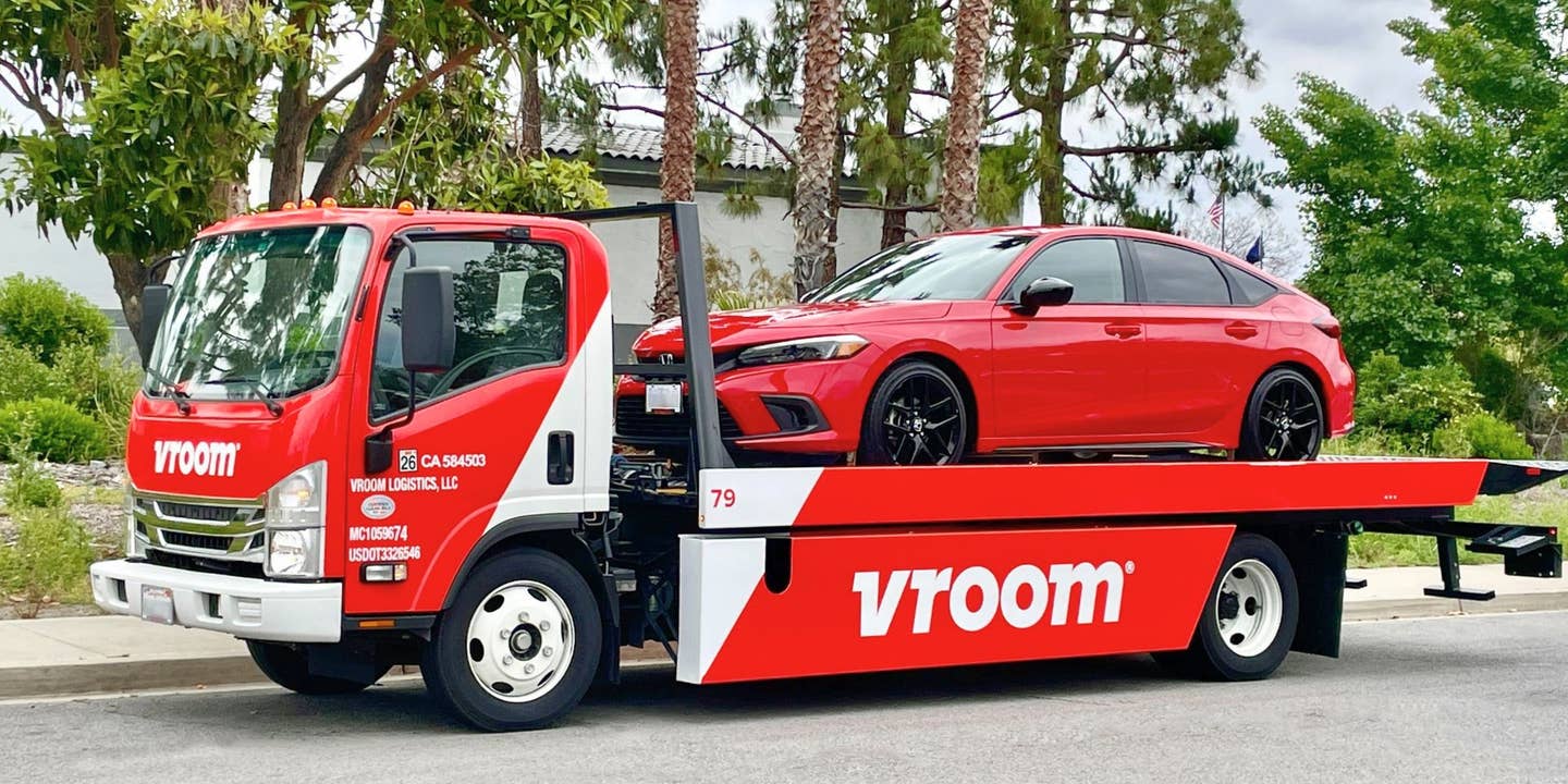 A red Honda Civic on the back of a flatbed track with prominent Vroom branding