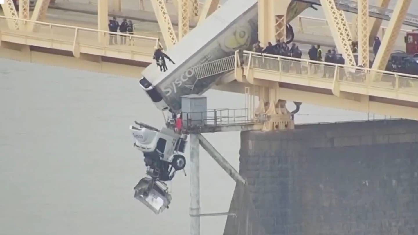 A semi truck dangles over the side of a bridge