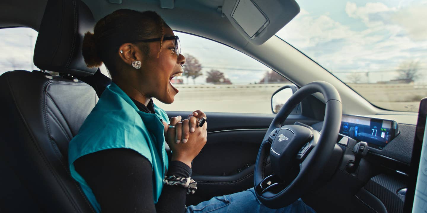 An excited driver clasps her hands in a Ford Mustang after activating BlueCruise, allowing her to remove her hands from the steering wheel.