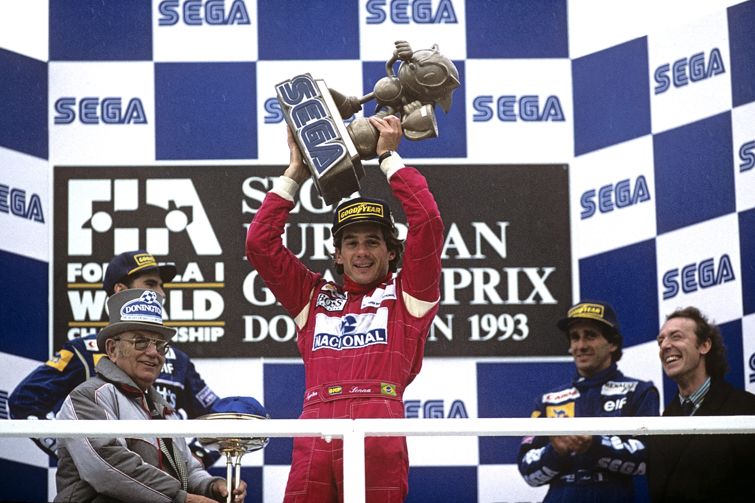 Senna stands on the top step of the podium hoisting a winner's trophy made in the image of Sonic the Hedgehog at the 1993 European Grand Prix at Donington, which Sega sponsored.