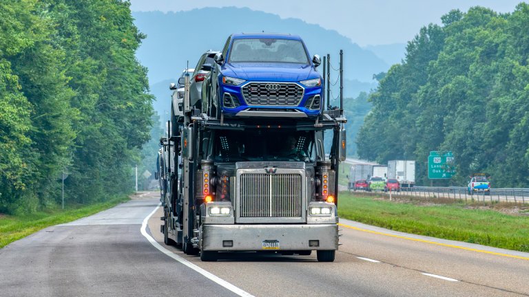 Audi being transported on top of a semi-truck car carrier.
