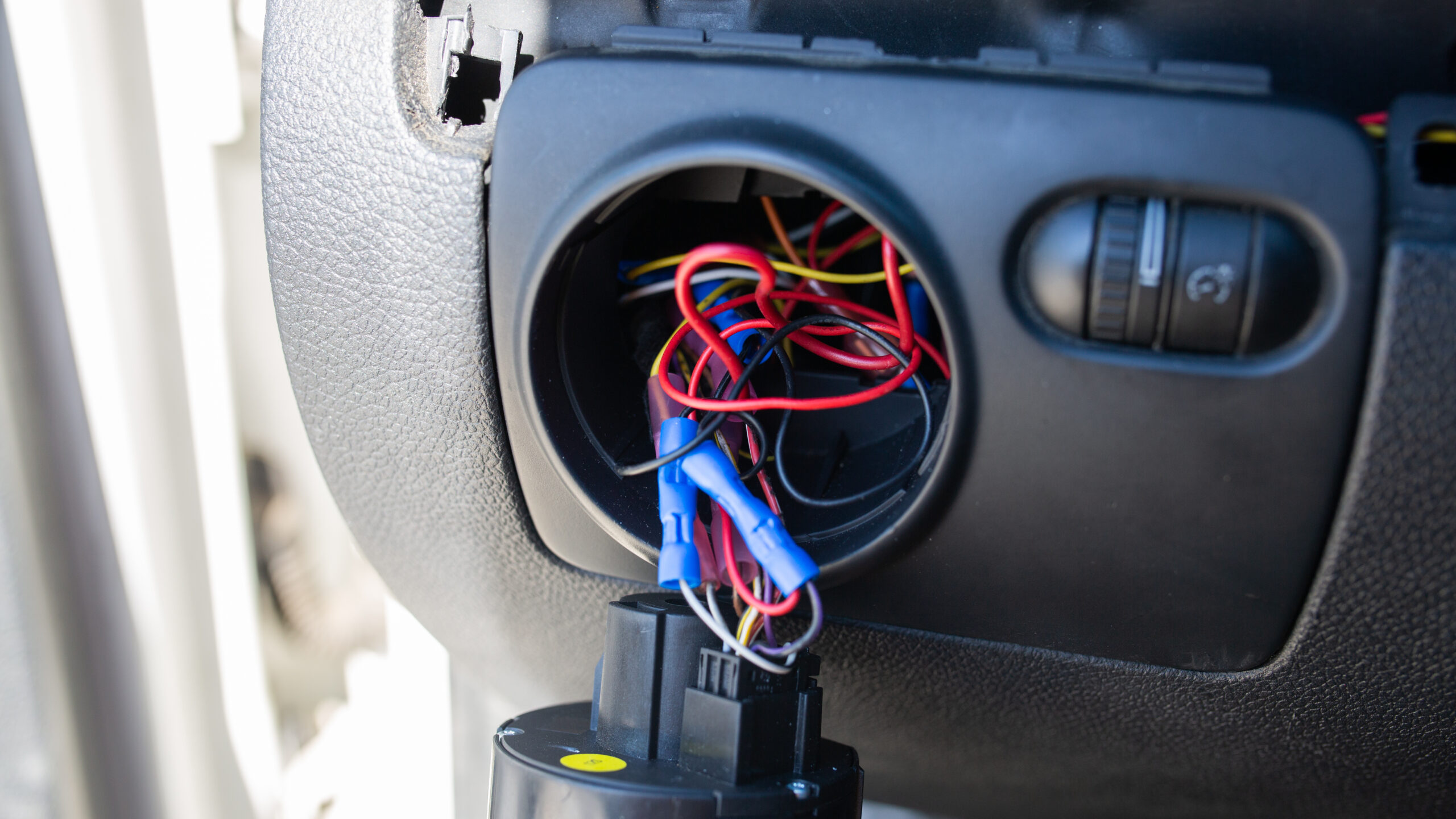 A bundle of wires within a circular cavity on the dashboard of a 2010 Volkswagen GTI. Dangling from the wires is a circular headlight switch.