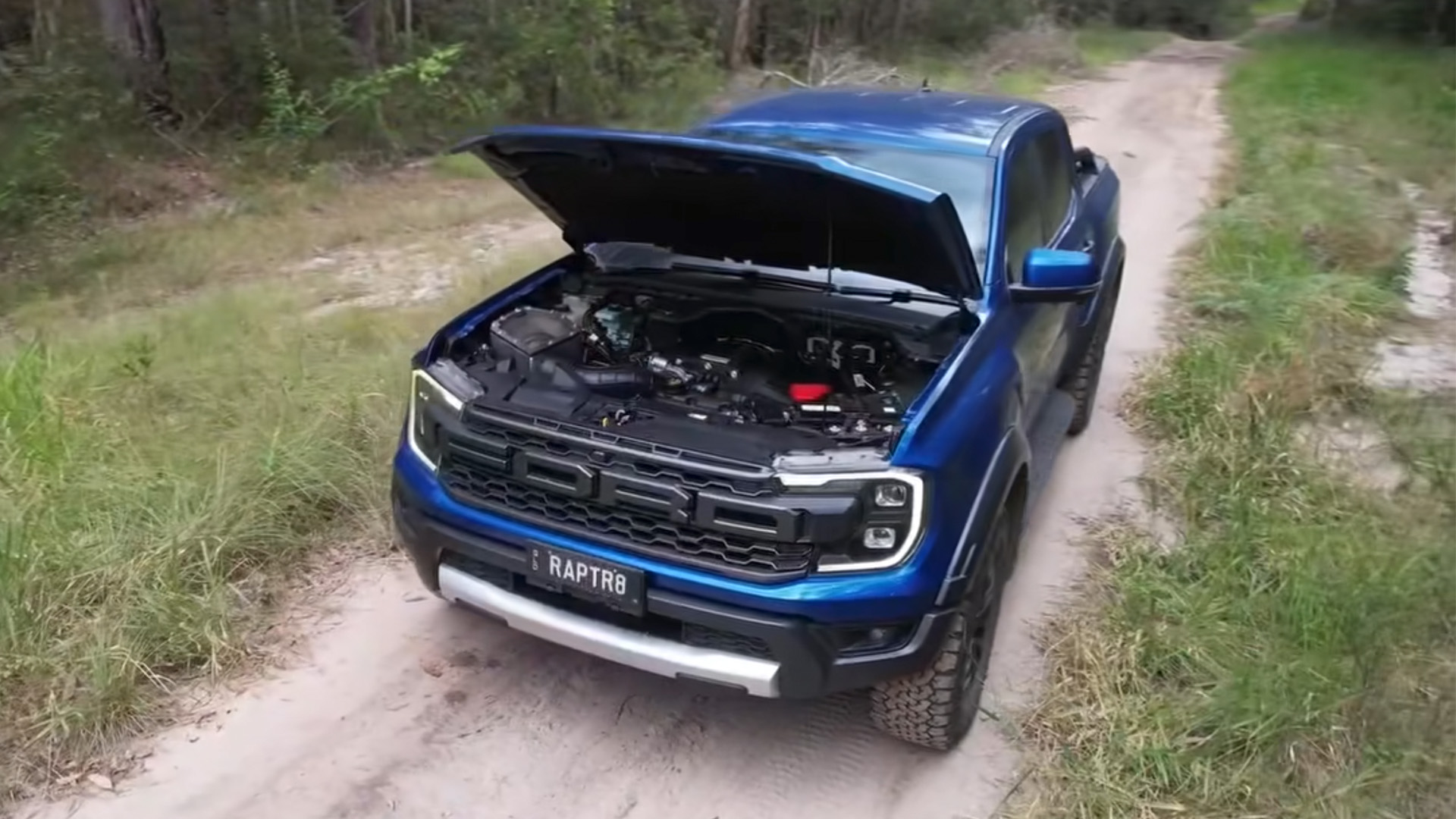 An engine-swapped Ford Ranger Raptor sits parked on a sandy trail.