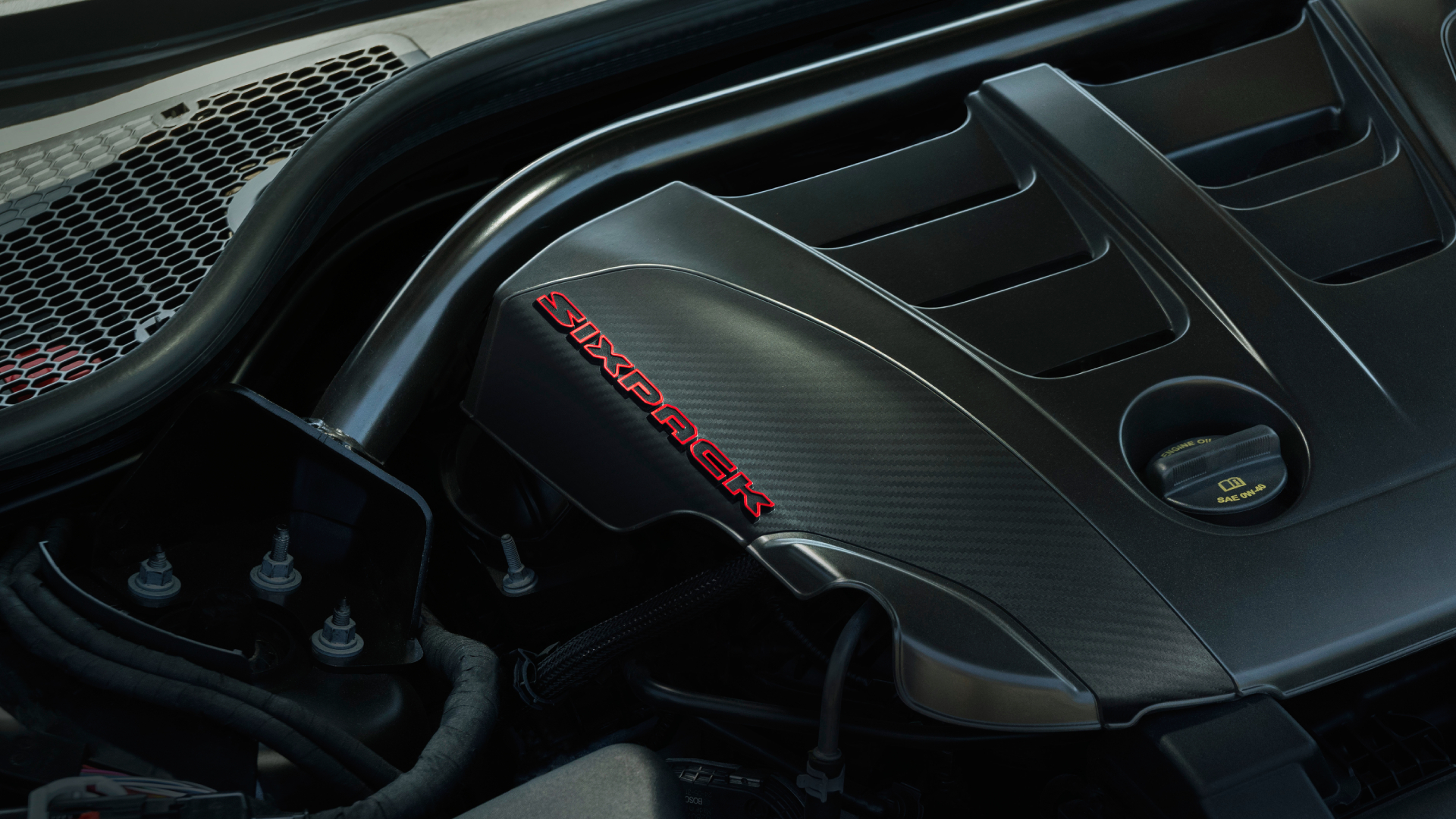 SIXPACK-powered Dodge Charger models feature a carbon-styled engine cover stamped with a red-accented SIXPACK text logo that announces the presence of the internal combustion engine under the hood.