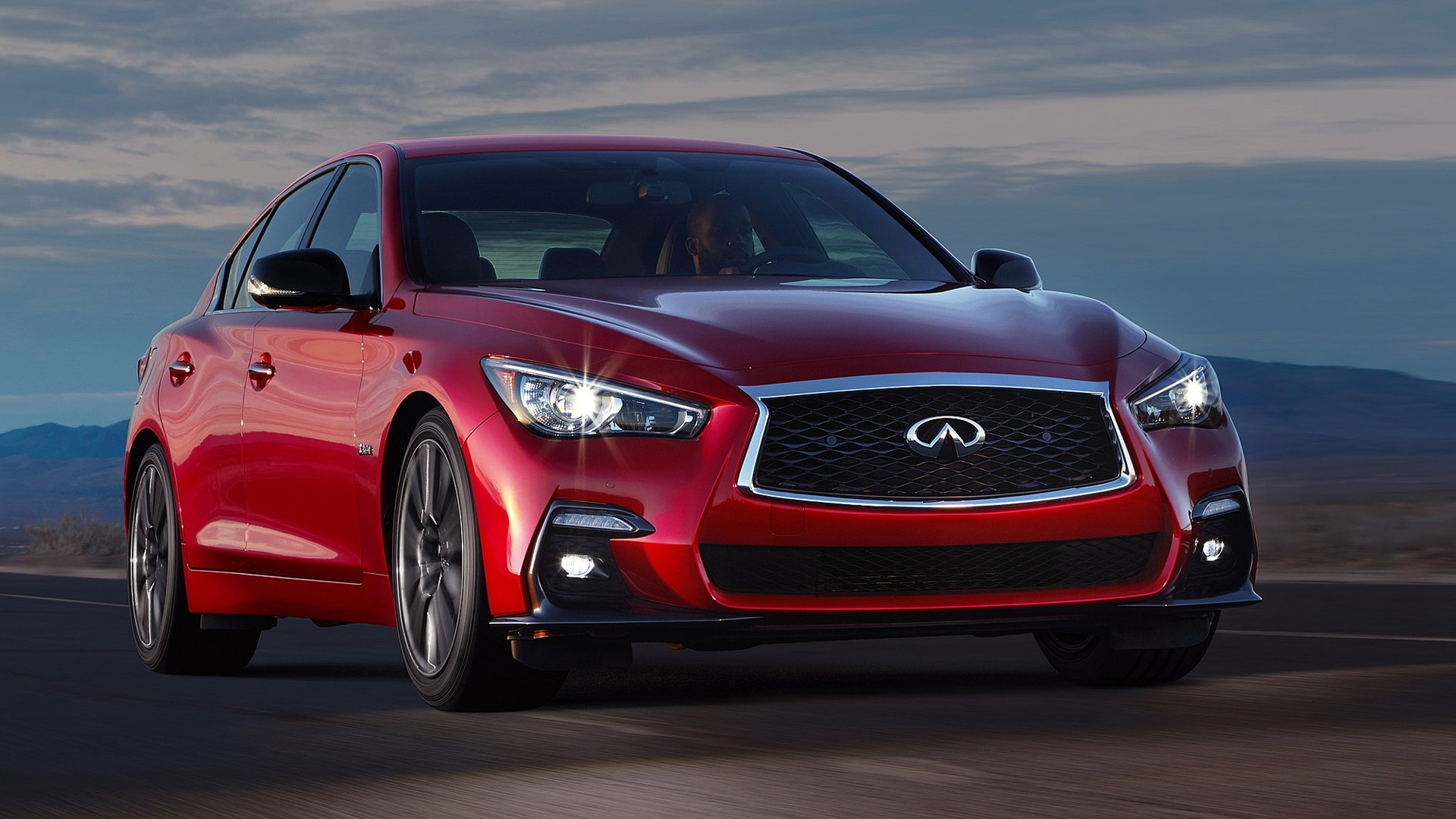 Infiniti Q50 moving across a dIesert road.